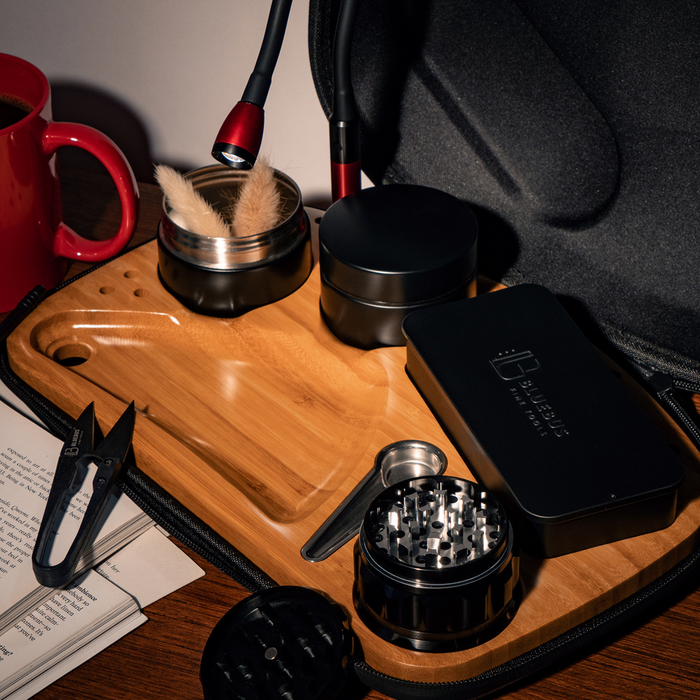 Wooden tray with smoking accessories including a grinder and black case on a table.