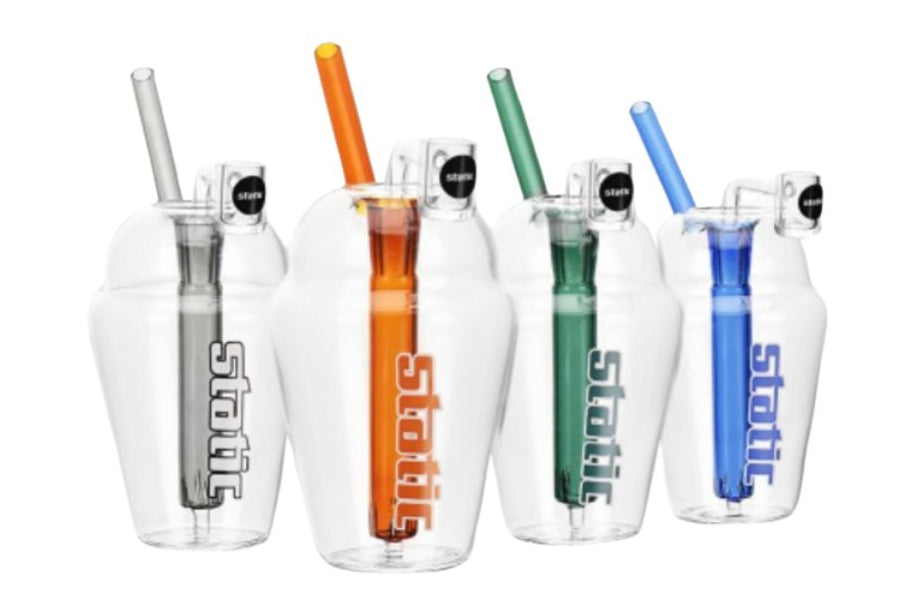 Four clear glass tumblers with integrated straws and lids, shown in different straw colors: silver, orange, green, and blue. The tumblers feature the brand name 'stott' printed vertically in white on the front.