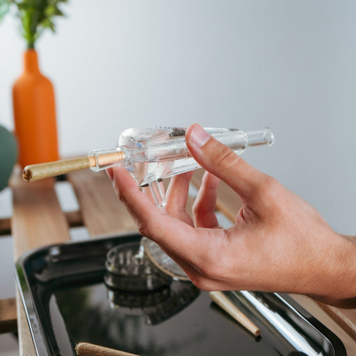 Hand holding a clear glass pipe with gold accent on a blurred background