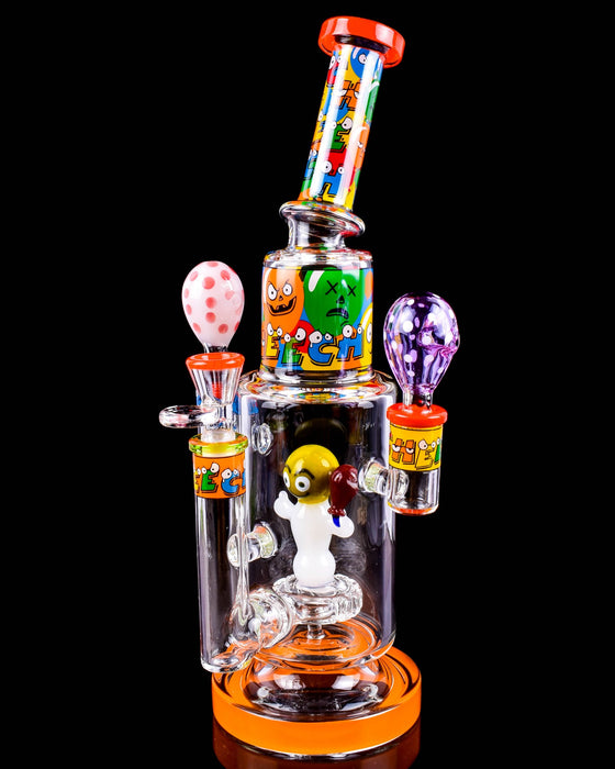 A clear glass water pipe with colorful cartoon monster graphics and multiple bulb-shaped mouthpieces in pink, orange, green, and purple, set against a solid black background.
