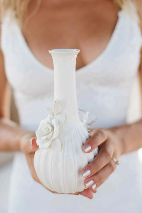 White vase with floral decorations held by a person wearing a white dress.