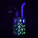 Glass water pipe with glowing green cannabis leaf patterns on a black background